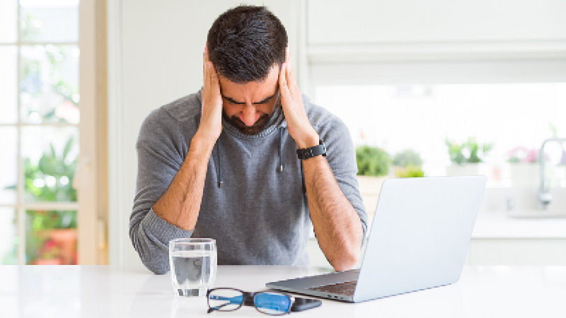 man holding head looking at laptop